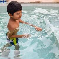 feliz indiano Garoto natação dentro uma piscina, criança vestindo natação traje ao longo com ar tubo durante quente verão Férias, crianças Garoto dentro grande natação piscina. foto