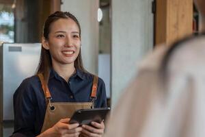 Ásia mulher proprietário feliz e sorrir receber ordem a partir de cliente. garantias segurança, limpeza, aberto a café fazer compras. aberto para Novo normal. pequeno negócios, Bem-vindo, restaurante, casa feito, cafeteria foto