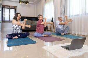 Senior ásia casal e filha estão exercício às casa fazendo sentado meditação ioga pose com conectados treinador classe a partir de Internet para mais velho saudável e longevidade conceito foto