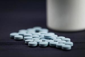 comprimidos de medicamentos em uma fileira contra um fundo de madeira. frasco de comprimido branco foto