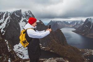 homem viajante tirando foto com smartphone caminhando no cume da montanha de Reinebringen, na Noruega, estilo de vida viajando