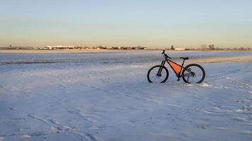 montanha bicicleta às inverno pôr do sol em uma campo coberto de neve com industrial área dentro fundo foto