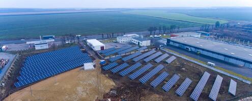 armazém telhado usava para a instalação do numerosos solar poder estações. Vila e agrícola campo às a pano de fundo. foto