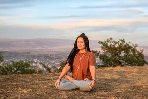 jovem mulher é sentado dentro a lótus posição e meditando em montanha topo. conceito do saudável estilo de vida. foto