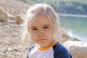 pequeno menina com loiro cabelo olhando às a Câmera com uma triste expressão em dela face foto