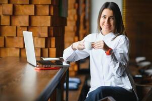 retrato do uma jovem fêmea trabalhador autonomo usando computador portátil computador para distância trabalho enquanto sentado dentro moderno café fazer compras interior, inteligente Loiras mulher trabalhando em netbook durante manhã café da manhã dentro cafeteria Barra foto