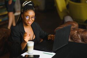satisfeito africano menina usando computador portátil às cafeteria, trabalhando on-line, cópia de espaço foto