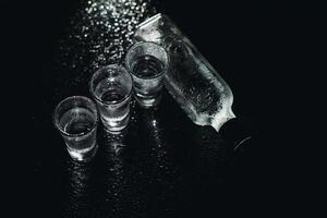 fechar-se Visão do garrafa e óculos do vodka em pé isolado em Preto. foto