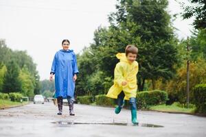 mãe e filho dentro capas de chuva ter Diversão juntos dentro a chuva. conceito do família período de férias e feliz infância. foto