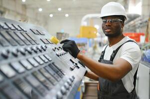 retrato do africano americano masculino engenheiro dentro uniforme e em pé dentro industrial fábrica foto