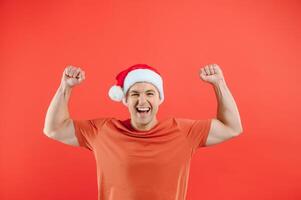 retrato do feliz e animado homem dentro santa chapéu, alegria e ganhando algo, a comemorar Novo ano, em pé sobre vermelho fundo foto