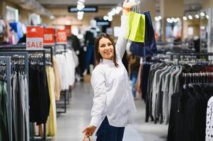 oferta, roupas , compras, moda e pessoas conceito - feliz jovem mulher escolhendo entre dois camisas dentro Shopping ou roupas loja foto