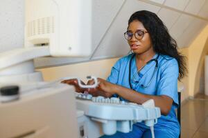 sorridente africano mulher médico com ultrassom scanner dentro mão, trabalhando em moderno ultrassom digitalização máquina dentro luz quarto dentro clínica. retrato do 4d ultrassom digitalização máquina operador foto