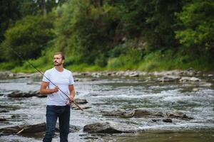 barbudo homem pegando peixe. verão lazer. maduro homem pescaria em a lago. retrato do alegre Senior homem pescaria. masculino pescaria. homem-peixe malha girar para dentro a rio esperando grande peixe foto