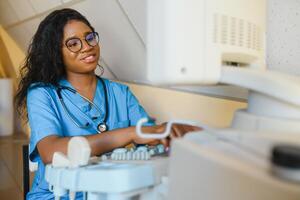 jovem alegre africano mulher operador do a ultrassom digitalização máquina analisando diagnóstico resultados do paciente. jovem sorridente africano médico trabalhando em uma moderno ultrassom equipamento. foto