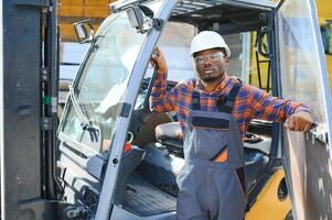 retrato do uma feliz africano americano masculino trabalhador dirigindo empilhadeira às local de trabalho foto