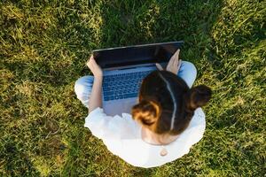 pequeno menina sentado em Relva e jogando tábua pc, tonificação foto. foto