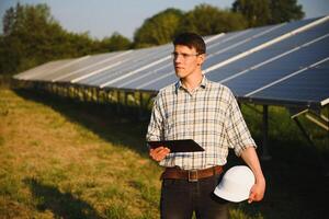 inspetor engenheiro homem segurando digital tábua trabalhando dentro solar painéis poder fazenda, fotovoltaico célula parque, verde energia conceito foto