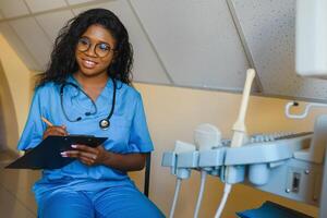 jovem alegre africano mulher operador do a ultrassom digitalização máquina analisando diagnóstico resultados do paciente. jovem sorridente africano médico trabalhando em uma moderno ultrassom equipamento. foto