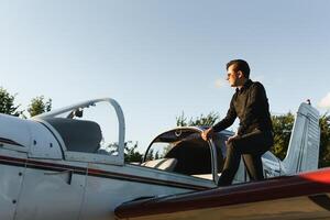 pensativo atraente jovem homem piloto em pé perto pequeno aeronave foto