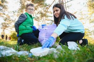 sorridente Garoto colheita acima Lixo dentro a parque com dele mãe. voluntário conceito. foto