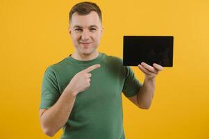 alegre jovem homem usando digital tábua em amarelo fundo foto