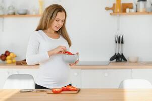 grávida mulher fatiamento legumes às casa dentro a cozinha foto