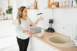 grávida mulher preparando café da manhã, cereais com leite e natural suco, dentro a cozinha. foto