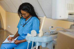 jovem alegre africano mulher operador do a ultrassom digitalização máquina analisando diagnóstico resultados do paciente. jovem sorridente africano médico trabalhando em uma moderno ultrassom equipamento. foto