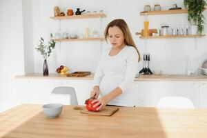 grávida mulher fatiamento legumes às casa dentro a cozinha foto