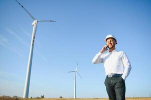 jovem homem de negocios falando para Gerente usando inteligente Telefone em vento turbina campo, verde energia conceito foto