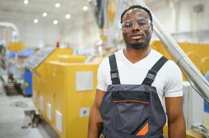 retrato do africano americano masculino engenheiro dentro uniforme e em pé dentro industrial fábrica foto