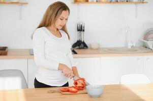 grávida mulher fatiamento legumes às casa dentro a cozinha foto