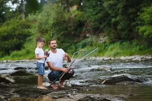 uma pai ensino dele filho quão para peixe em uma rio lado de fora dentro verão luz do sol. do pai dia. foto