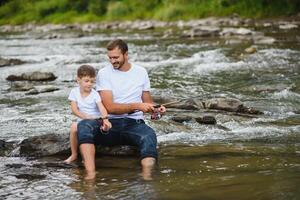 uma pai ensino dele filho quão para peixe em uma rio lado de fora dentro verão luz do sol. do pai dia. foto