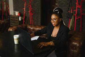 jovem africano americano mulher localização às cafeteria trabalhando em computador portátil foto