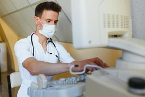 masculino médico dentro mascarar com ultrassom equipamento parece às a monitor dentro a clínica escritório foto