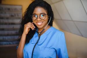 bonita fêmea africano médico com braços cruzado às hospital foto