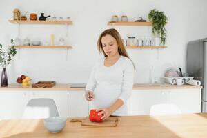 grávida mulher fatiamento legumes às casa dentro a cozinha foto