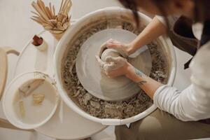 fêmea oleiro dentro avental fazer forma do argila vaso em fiação cerâmica ferramenta dentro cerâmico oficina foto