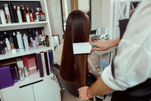 estilista de cabelo escovar grandes e lustroso Castanho cabelo do fêmea cliente às beleza salão foto