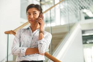 atraente empresária falando telefone com cliente enquanto em pé dentro escritório em escadas foto
