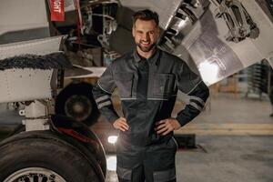 alegre masculino mecânico em pé perto avião dentro hangar foto