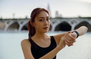 jovem mulher dentro roupa de esporte olhando em relógio inteligente antes exercício. ao ar livre Esportes dentro a manhã foto