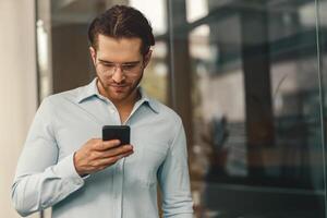 bonito masculino trabalhador autonomo segurando telefone enquanto em pé dentro escritório durante pausa Tempo foto