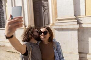 feliz turista casal caminhando dentro cidade rua, se beijando e fazer selfie em telefone foto