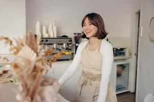 retrato do uma feliz fêmea barista em pé atrás a contador dentro uma café fazer compras foto