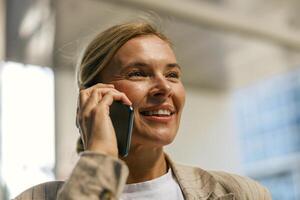 fechar acima do maduro o negócio mulher falando telefone com cliente em moderno construção fundo foto