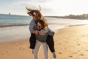 bonito casal dentro amor abraçando enquanto caminhando ao longo a de praia em ensolarado ventoso dia foto