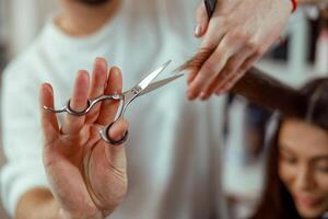 fechar acima do cabeleireiro mãos segurando uma cabelo vertente enquanto corte cabelo do fêmea cliente foto